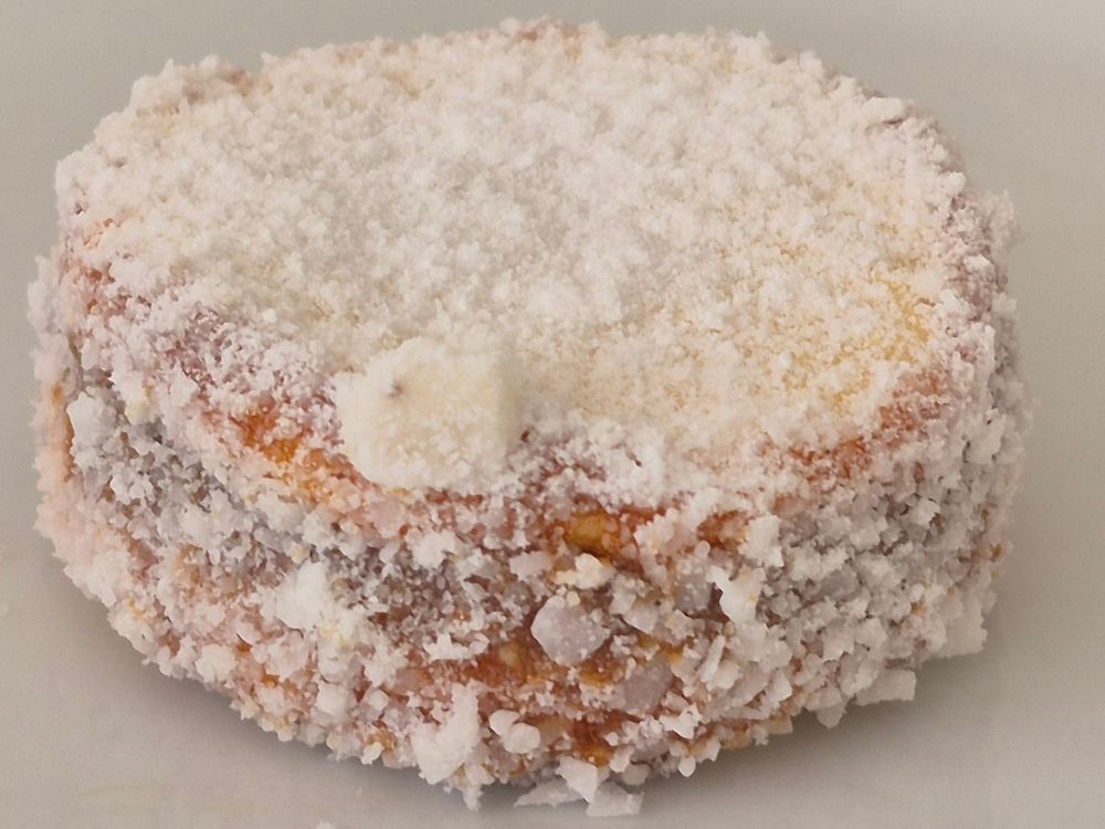 Primer plano de un alfajor de coco: el borde cubierto de coco rallado y la tapa con azúcar glass