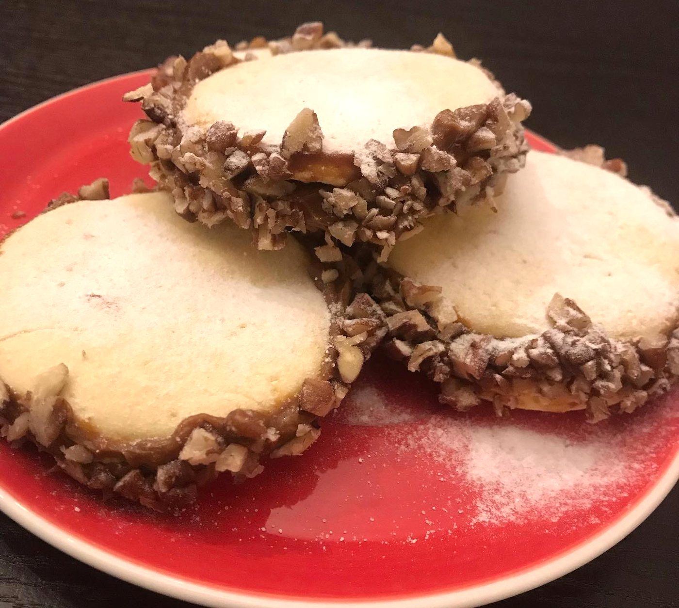 Tres alfajores de nuez en un plato rojo sobre madera oscura